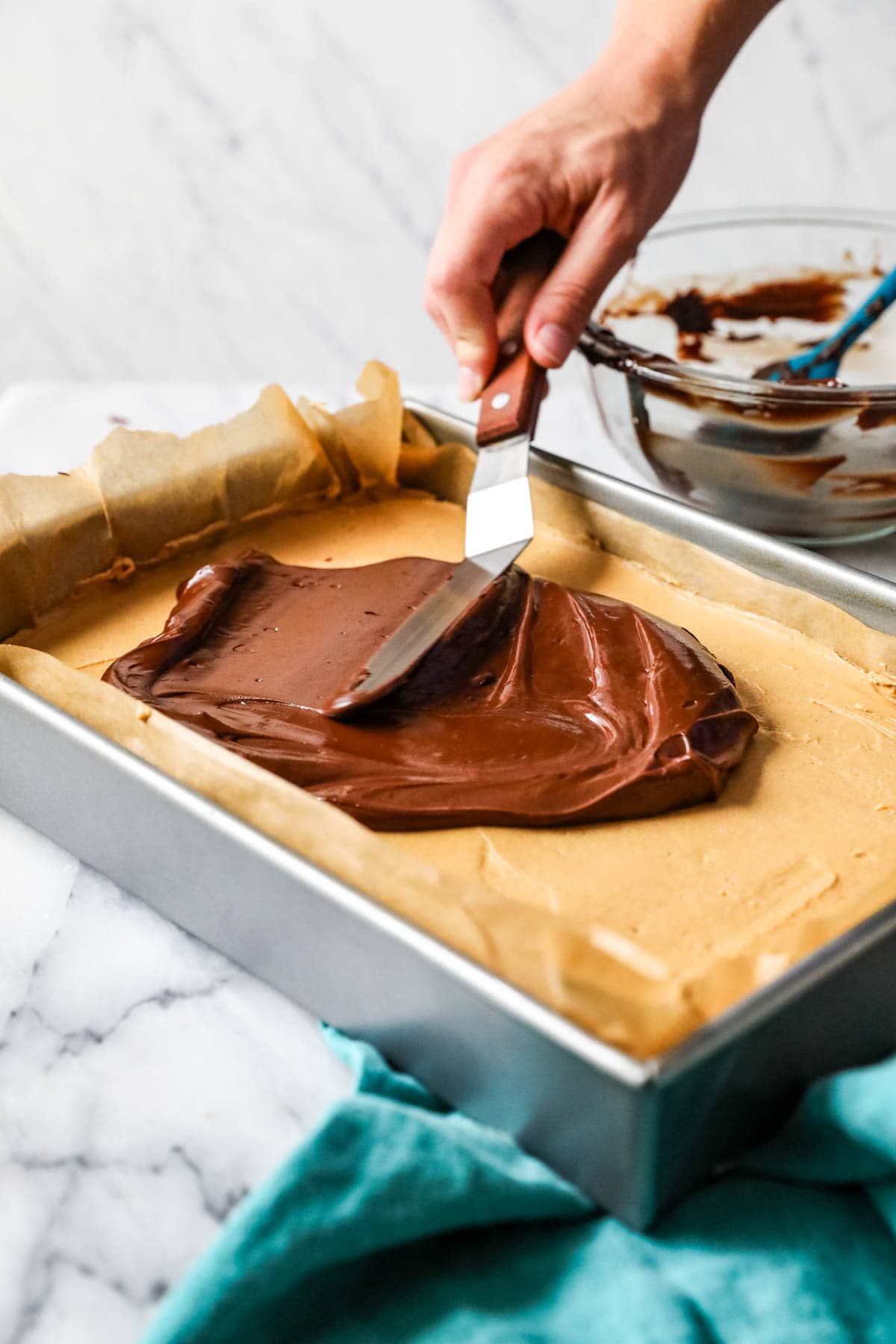 Chocolate being spread over peanut butter fudge with an offset spatula.