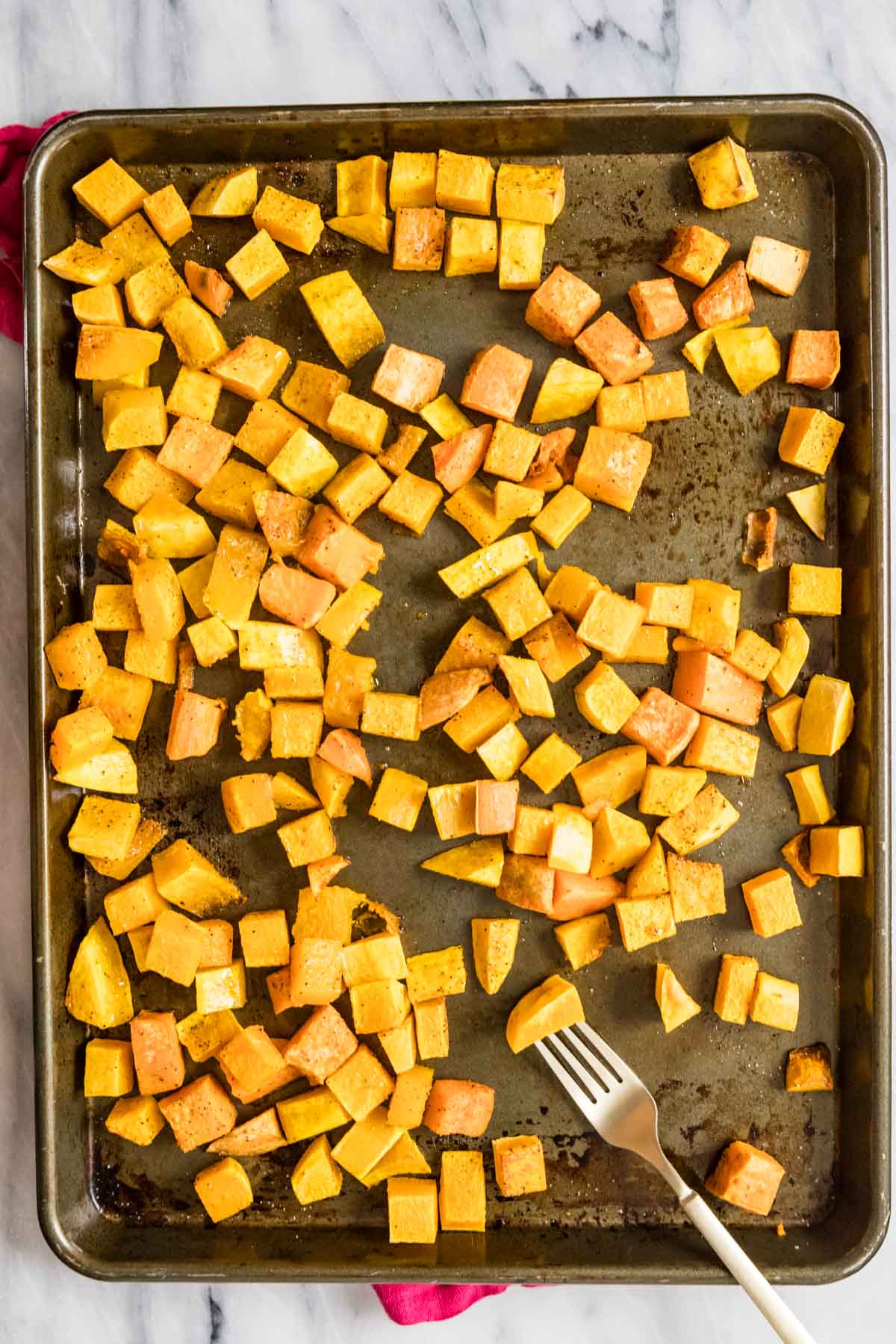 Overhead view of cubed butternut squash on a baking sheet.