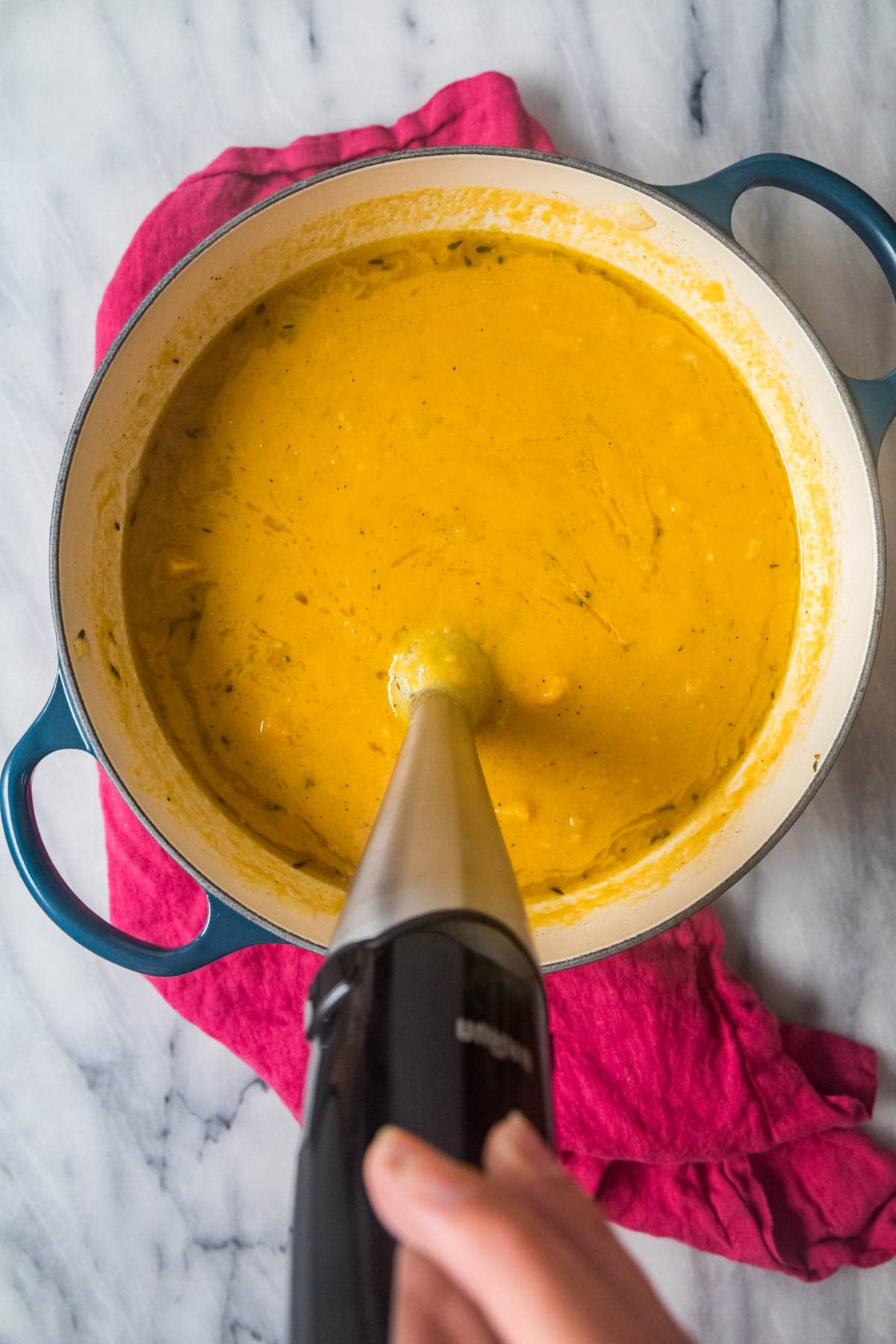 Overhead view of an immersion blender blending butternut squash soup.