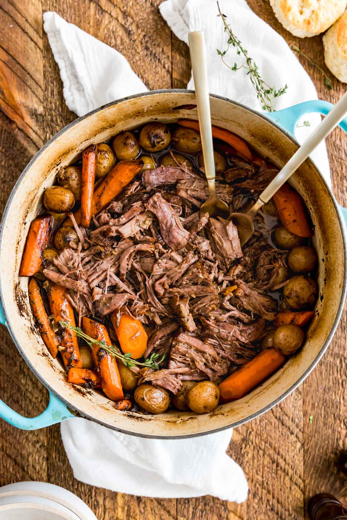 Two forks in a blue Dutch oven with shredded beef, carrots, and baby potatoes inside.