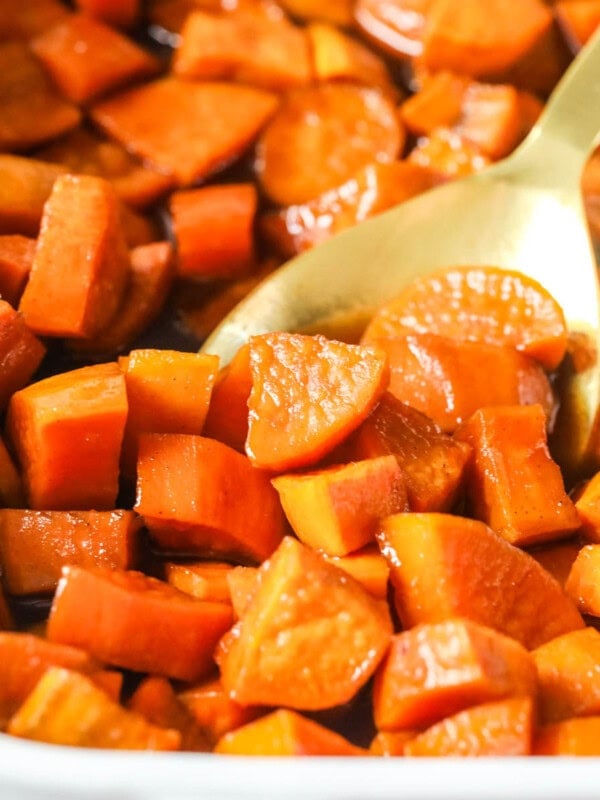 Casserole dish of candied yams with a gold spoon scooping a serving.