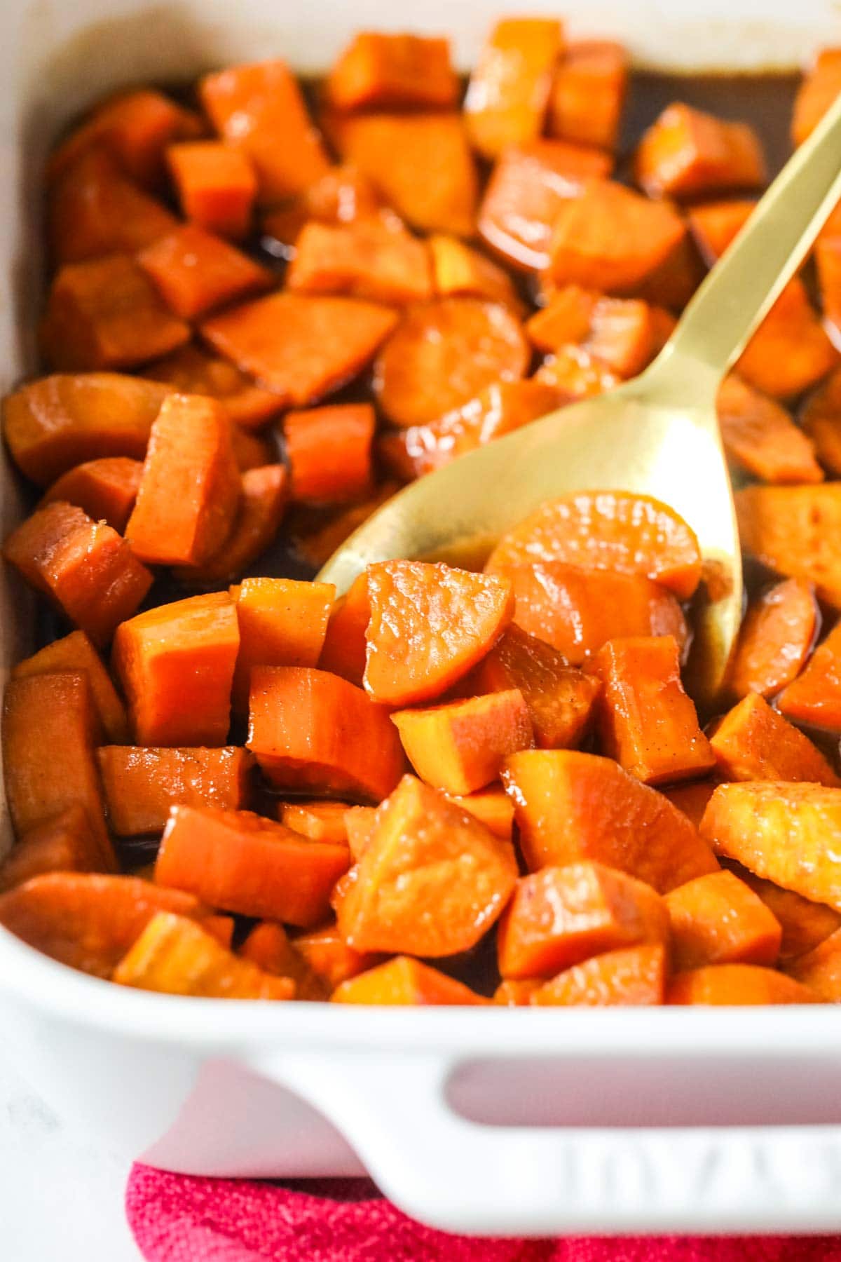 Casserole dish of candied yams with a gold spoon scooping a serving.