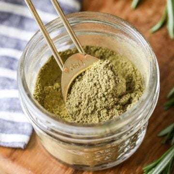 Overhead view of a small jar of homemade poultry seasoning with a gold measuring spoon inside.