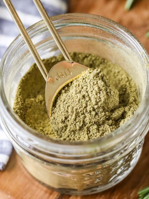 Overhead view of a small jar of homemade poultry seasoning with a gold measuring spoon inside.