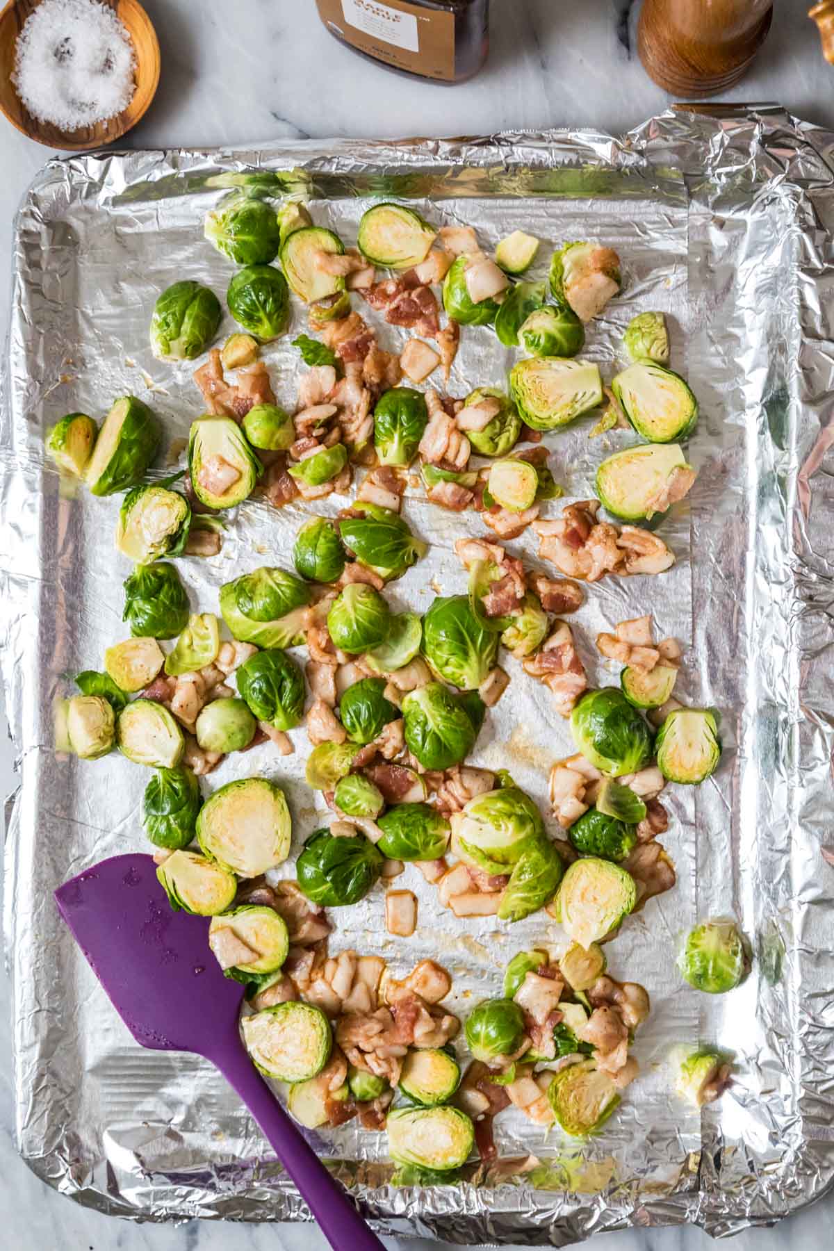 Overhead view of a foil lined baking sheet with brussels sprouts and bacon on it.