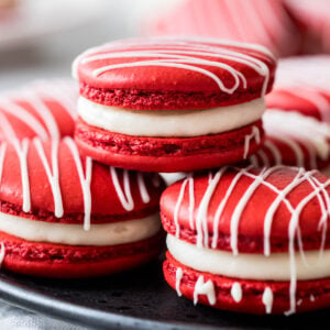 Three red velvet macarons stacked in a pyramid shape with more macarons behind.