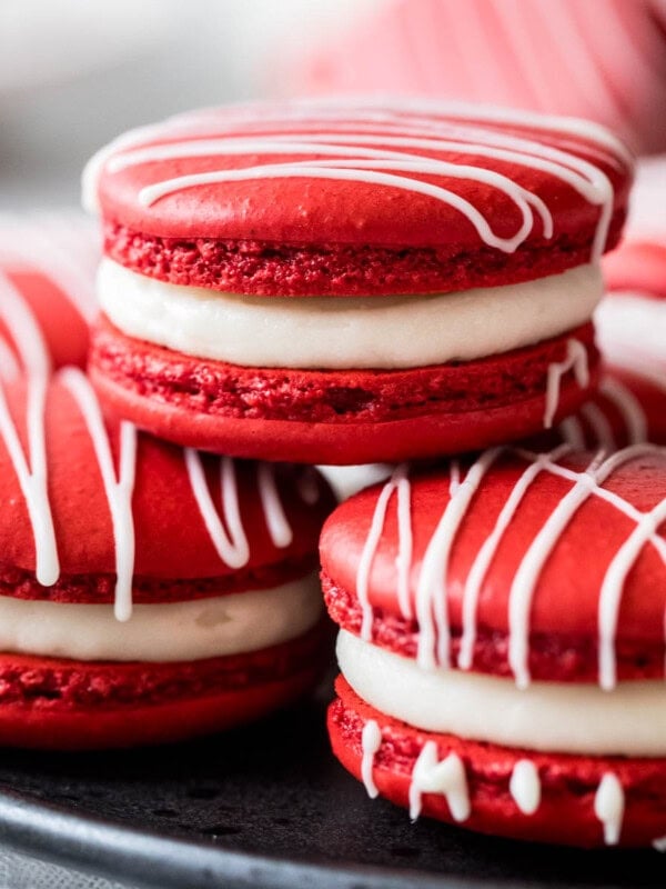 Three red velvet macarons stacked in a pyramid shape with more macarons behind.