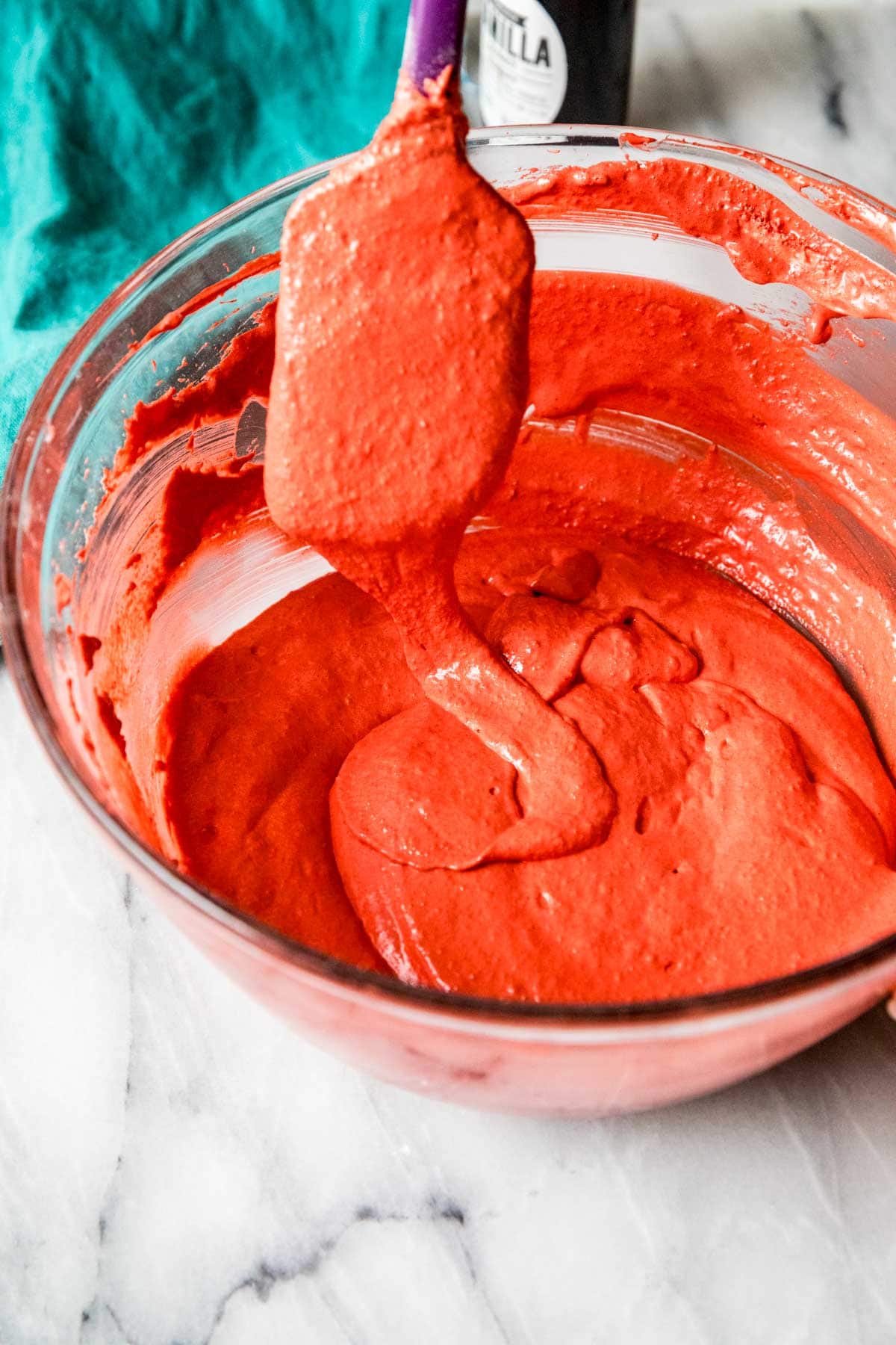 Red macaron batter ribboning off a spatula back into the bowl of batter.