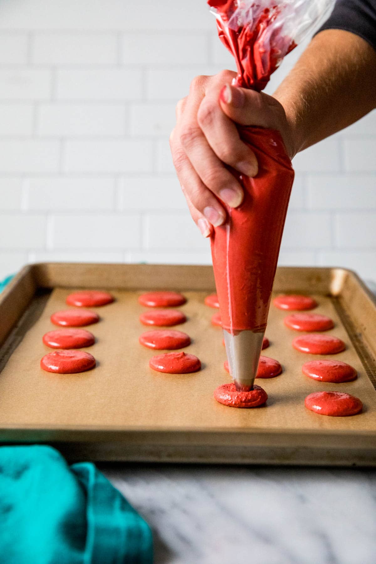 Red macaron batter being piped onto a baking sheet.