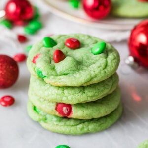 Stack of grinch cookies dyed a pale green color and decorated with red and green m&m candies.
