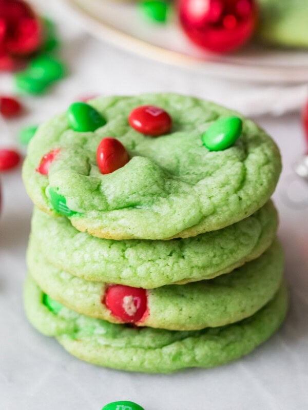 Stack of grinch cookies dyed a pale green color and decorated with red and green m&m candies.