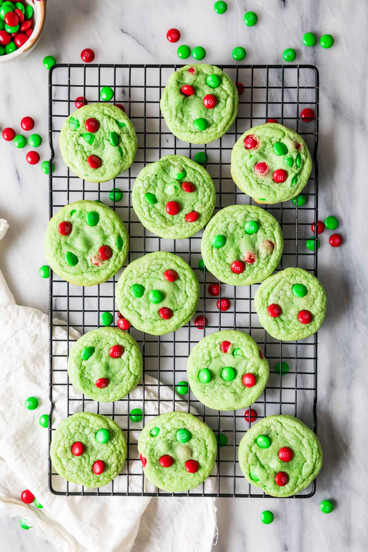 Overhead view of pale green cookies topped with red and green candies on a metal cooling rack.