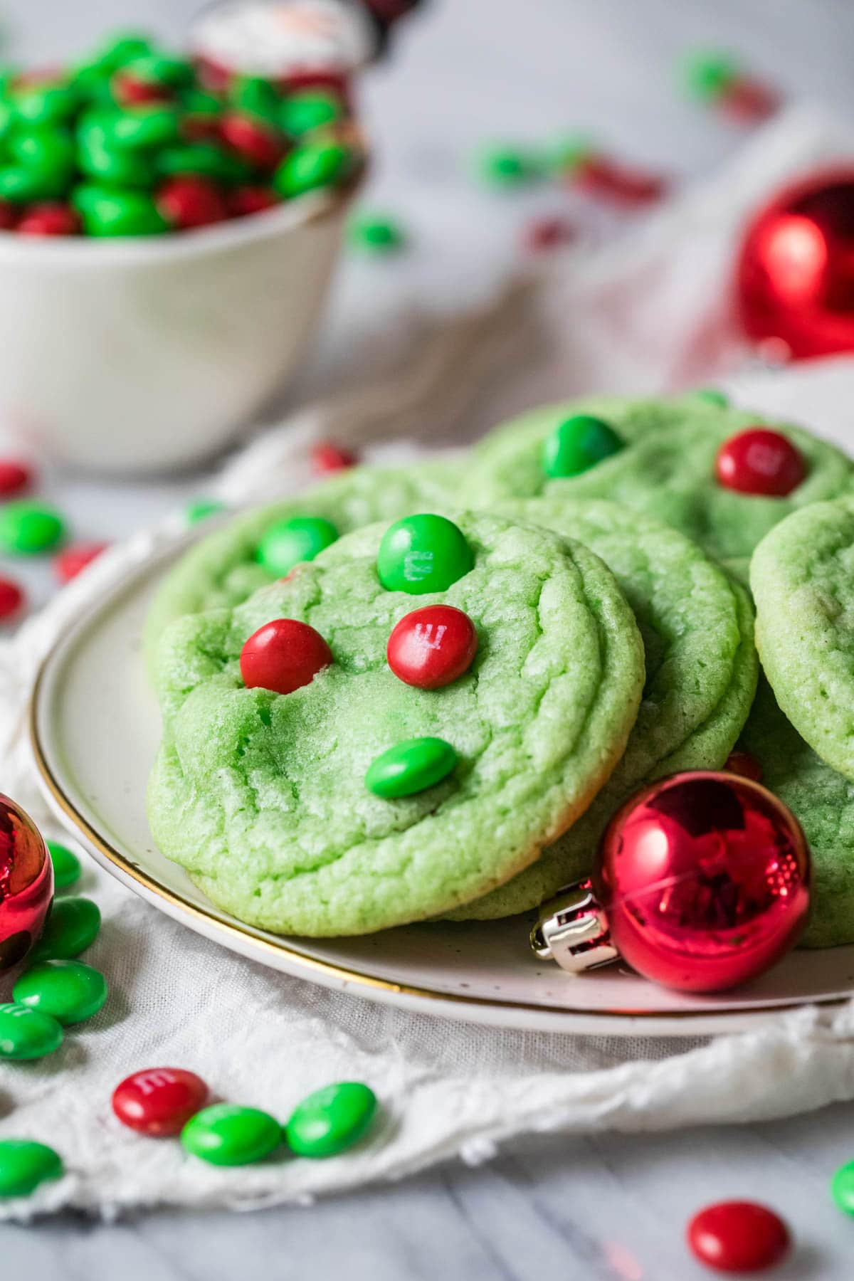 Grinch cookies arranged on a white plate with a red Christmas ornament in the front.
