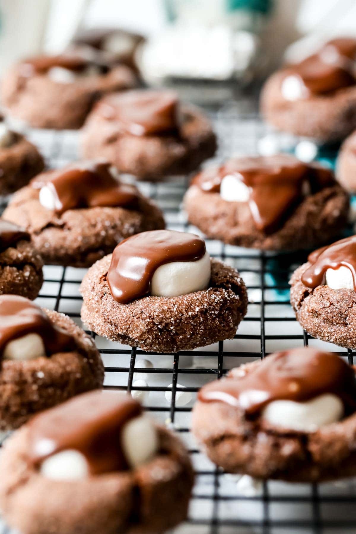 Close-up view of hot chocolate cookies topped with marshmallow and chocolate ganache on a cooling rack.