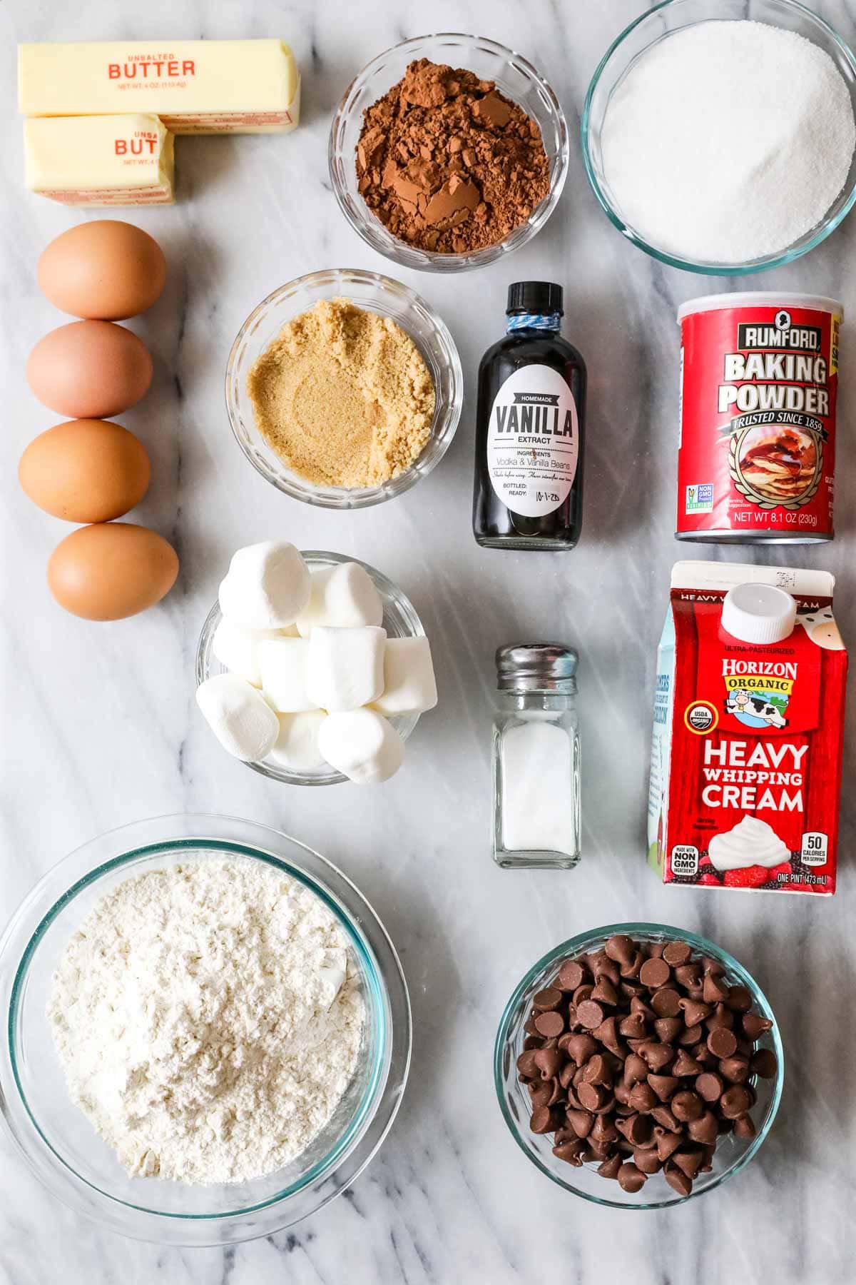 Overhead view of ingredients including cocoa powder, eggs, chocolate chips, marshmallows, and more.