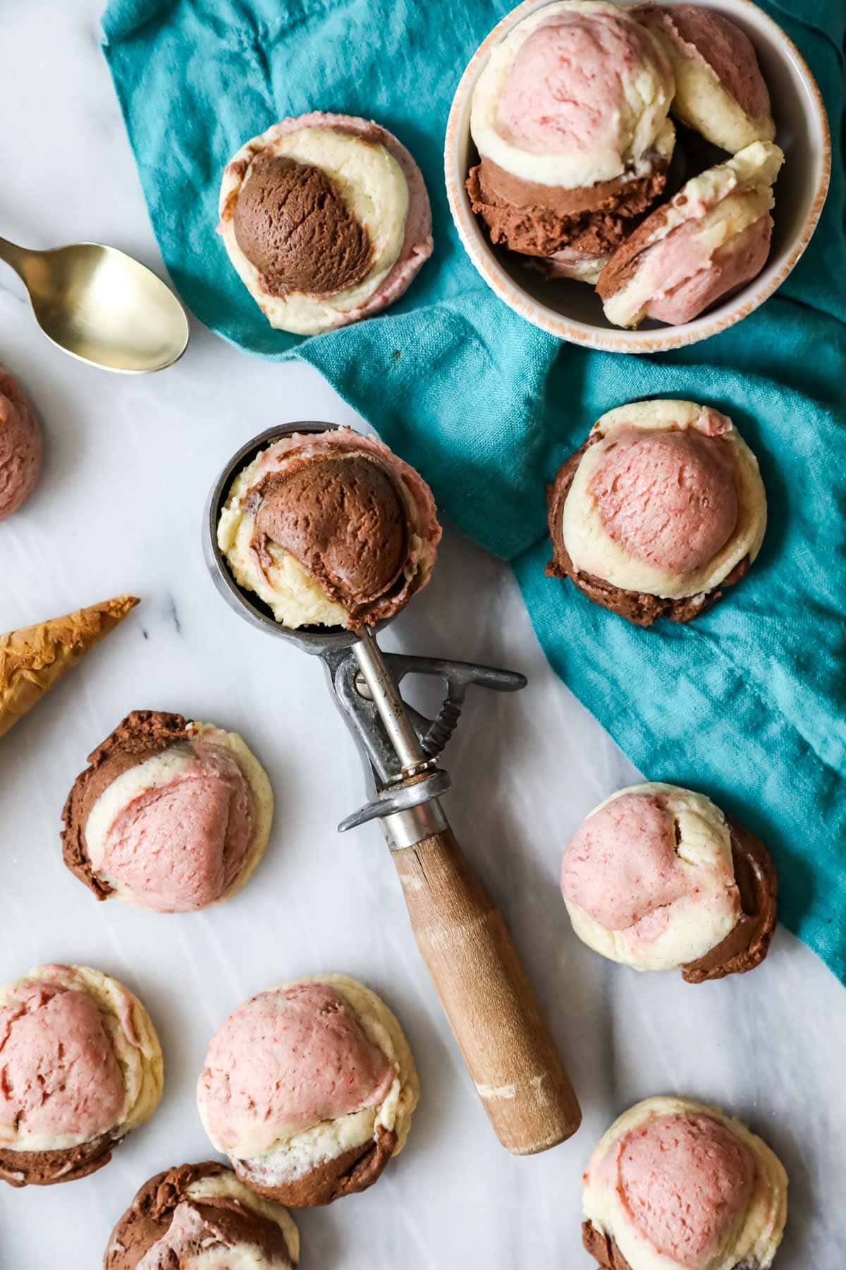 Neapolitan cookies scattered across a countertop with one cookie resting in an ice cream scoop.