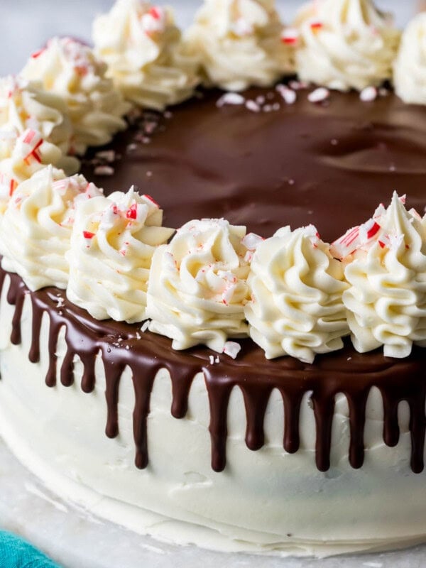 Peppermint bark cake decorated with chocolate ganache drip, white chocolate buttercream swirls, and crushed candy canes.