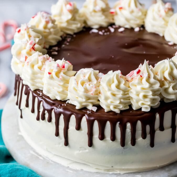 Peppermint bark cake decorated with chocolate ganache drip, white chocolate buttercream swirls, and crushed candy canes.