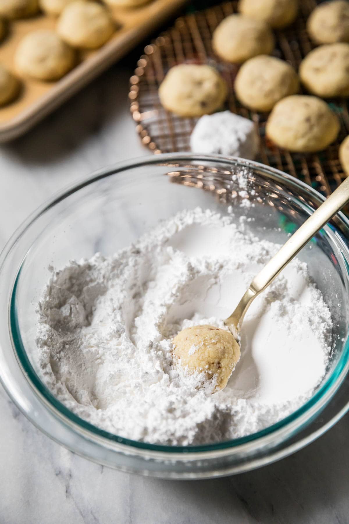 Cookie on a fork in a bowl of powdered sugar.