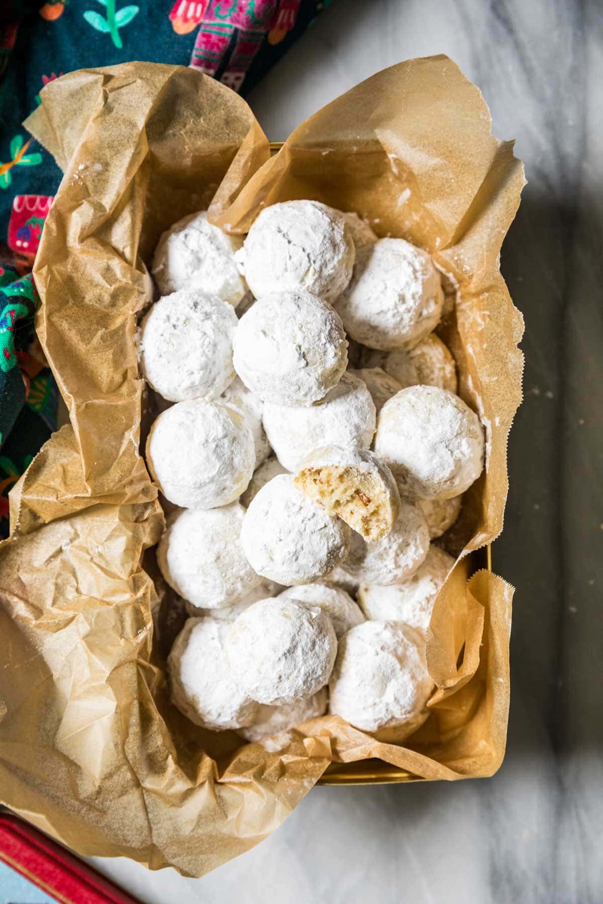 Overhead view of snowball cookies in a parchment lined bread pan with one cookie missing a bite.