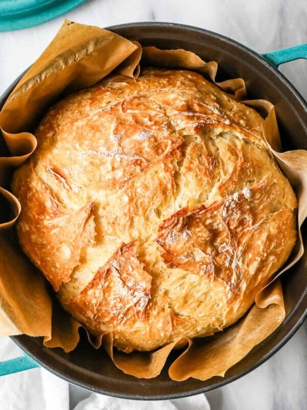 Overhead view of a round loaf of artisan bread in a teal dutch oven.