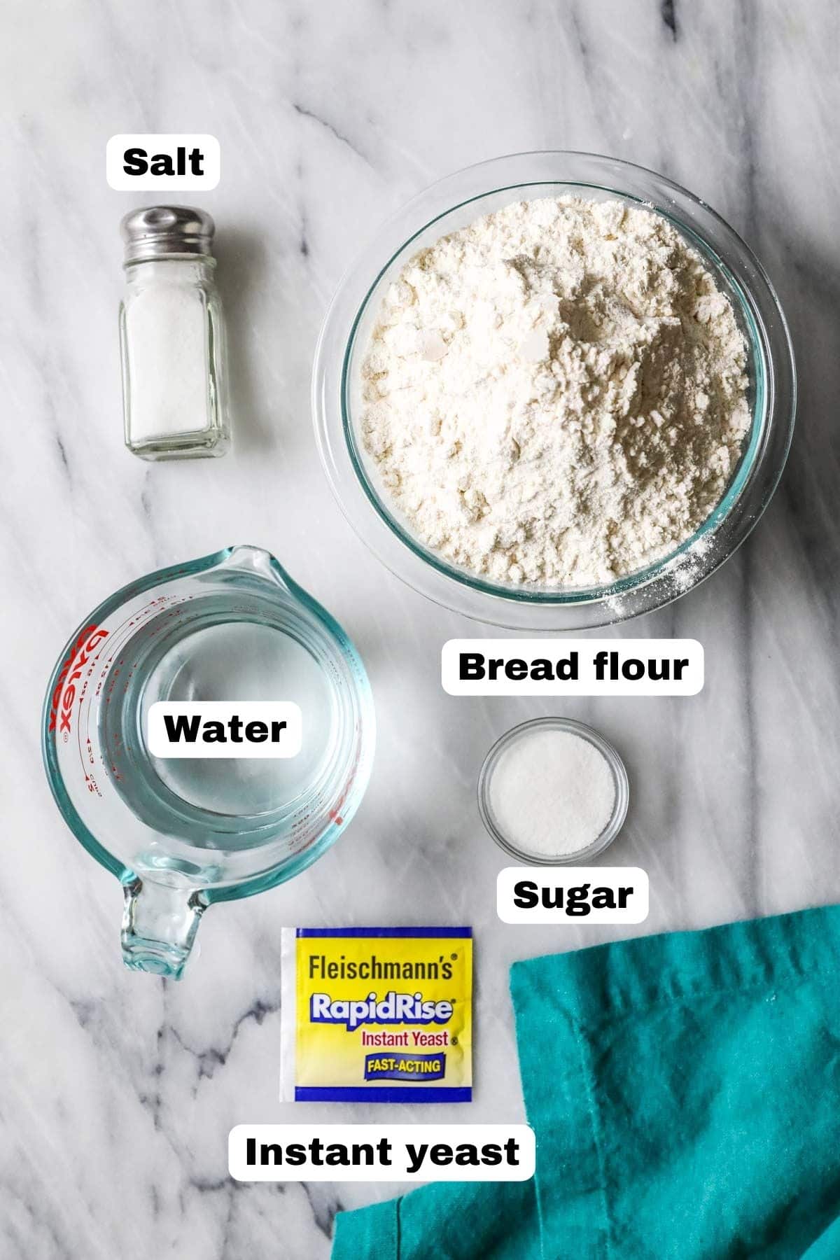 Overhead view of labelled ingredients including flour, yeast, sugar, water, and salt.