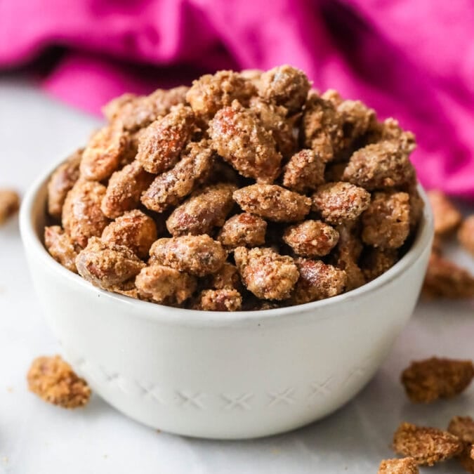 White bowl of candied almonds with a bright pink tea towel in the background.