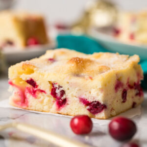 Square slice of cranberry cake with fresh cranberries in the foreground.