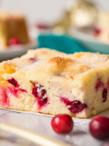 Square slice of cranberry cake with fresh cranberries in the foreground.