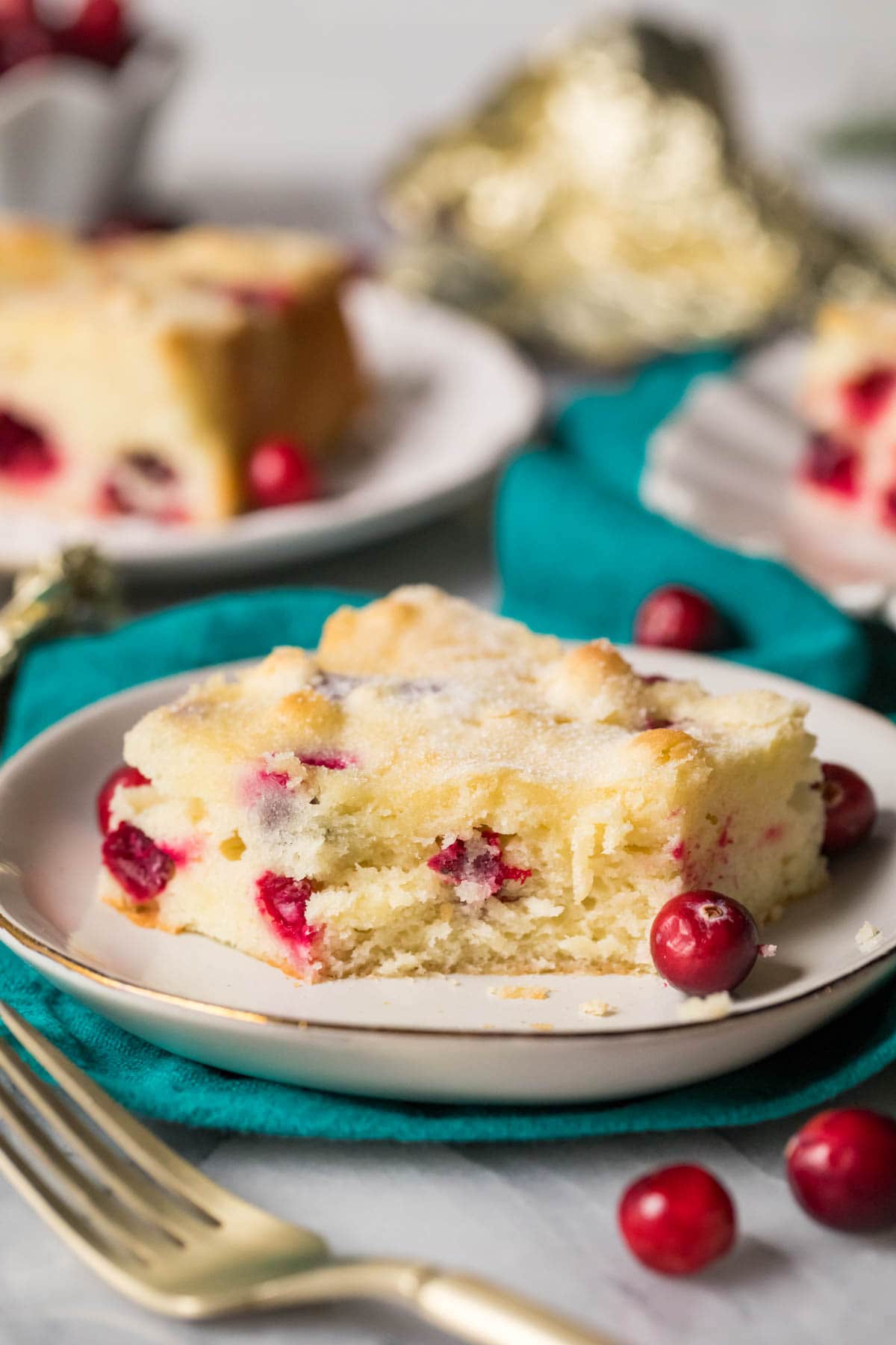 Square slice of cake made with fresh cranberries on a plate with one bite missing.