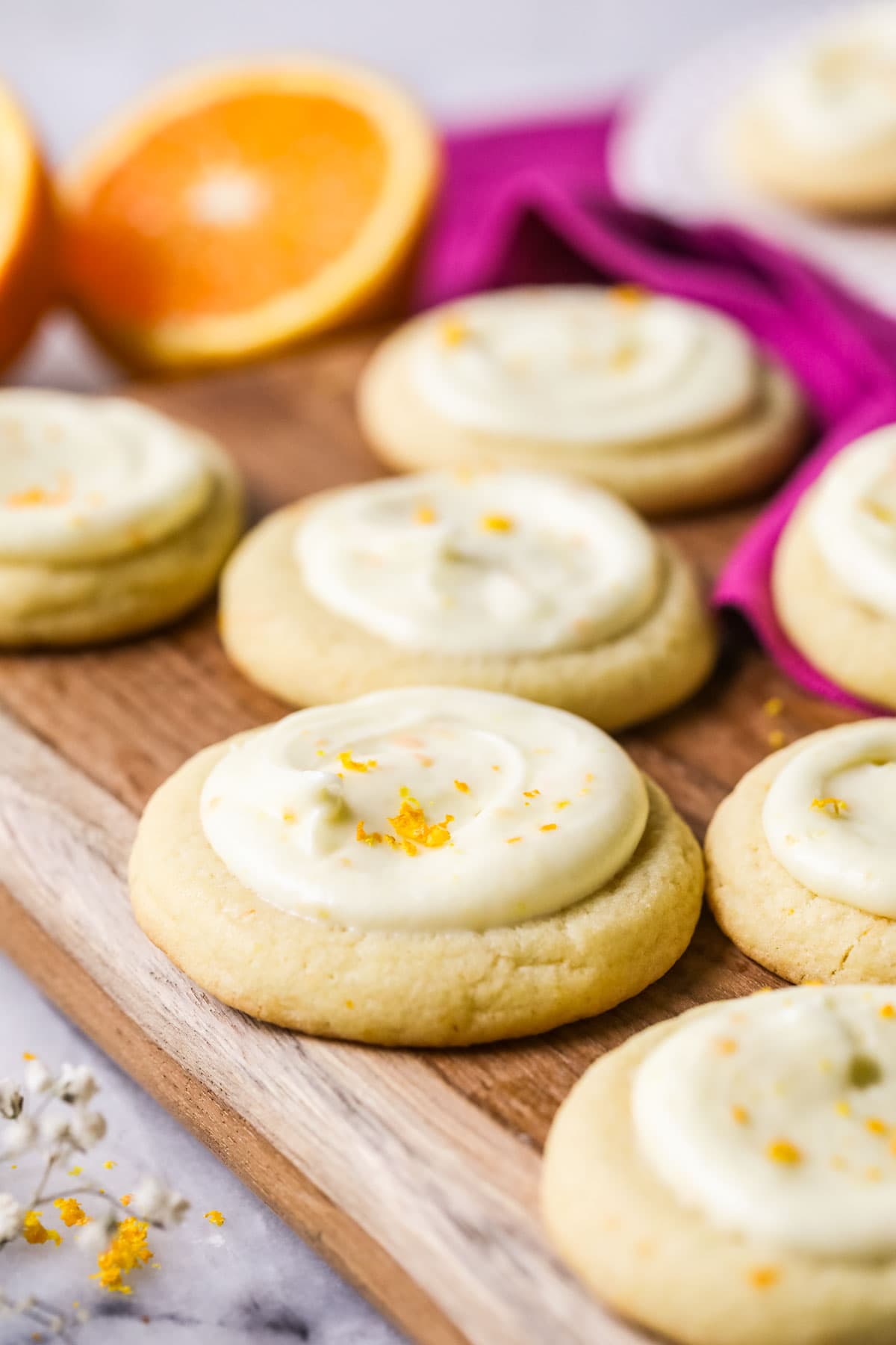 Orange flavored cookies topped with frosting and fresh orange zest on a wood cutting board.