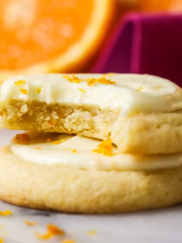 Two orange cookies stacked on top of each other with the top cookie missing one bite.