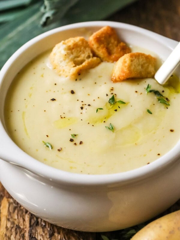 Small white crock of potato leek soup topped with croutons and chives.