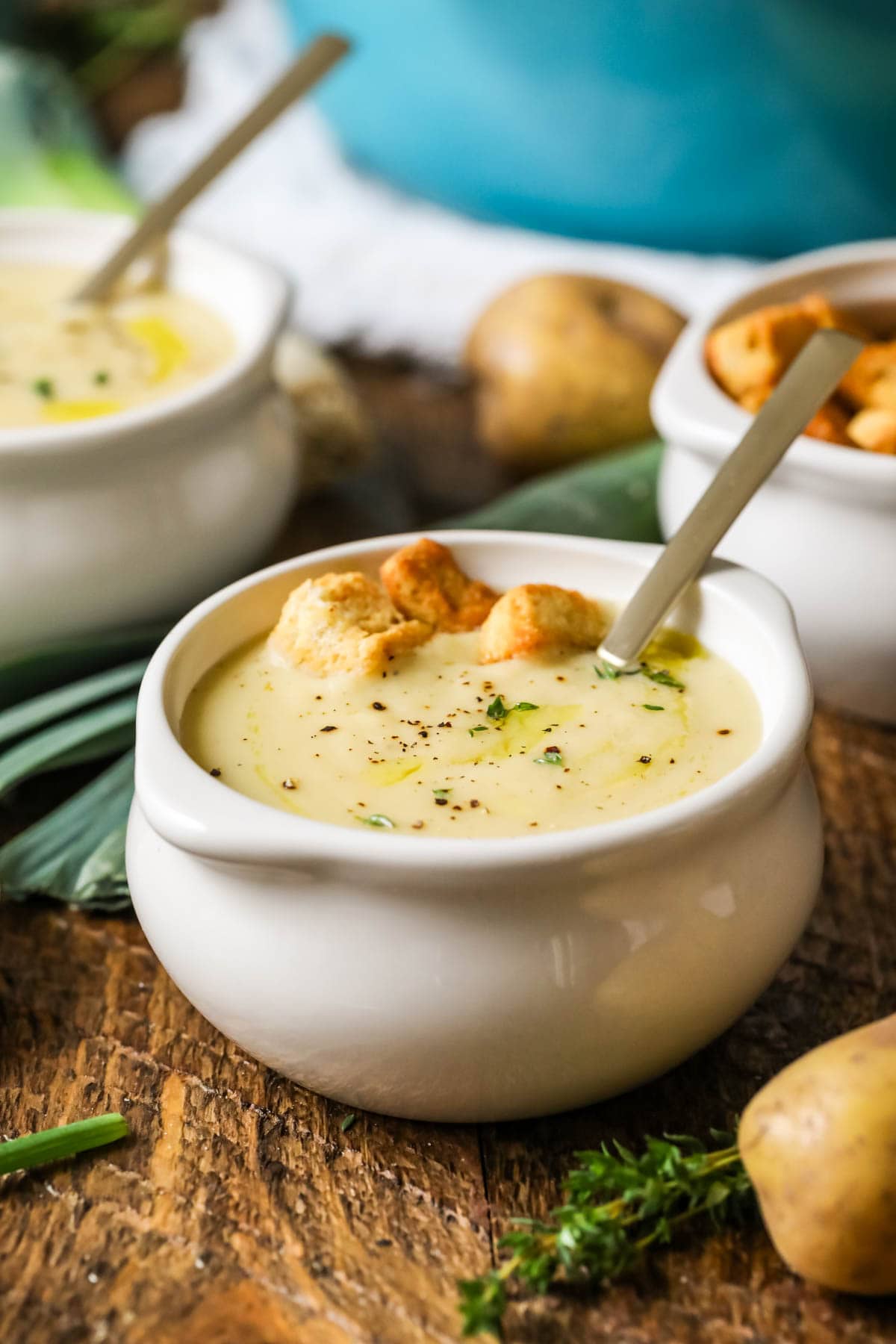 Small white crock of potato leek soup topped with croutons and chives.