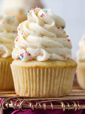 Vanilla cupcakes topped with tall swirls of vanilla bean buttercream on a cooling rack.