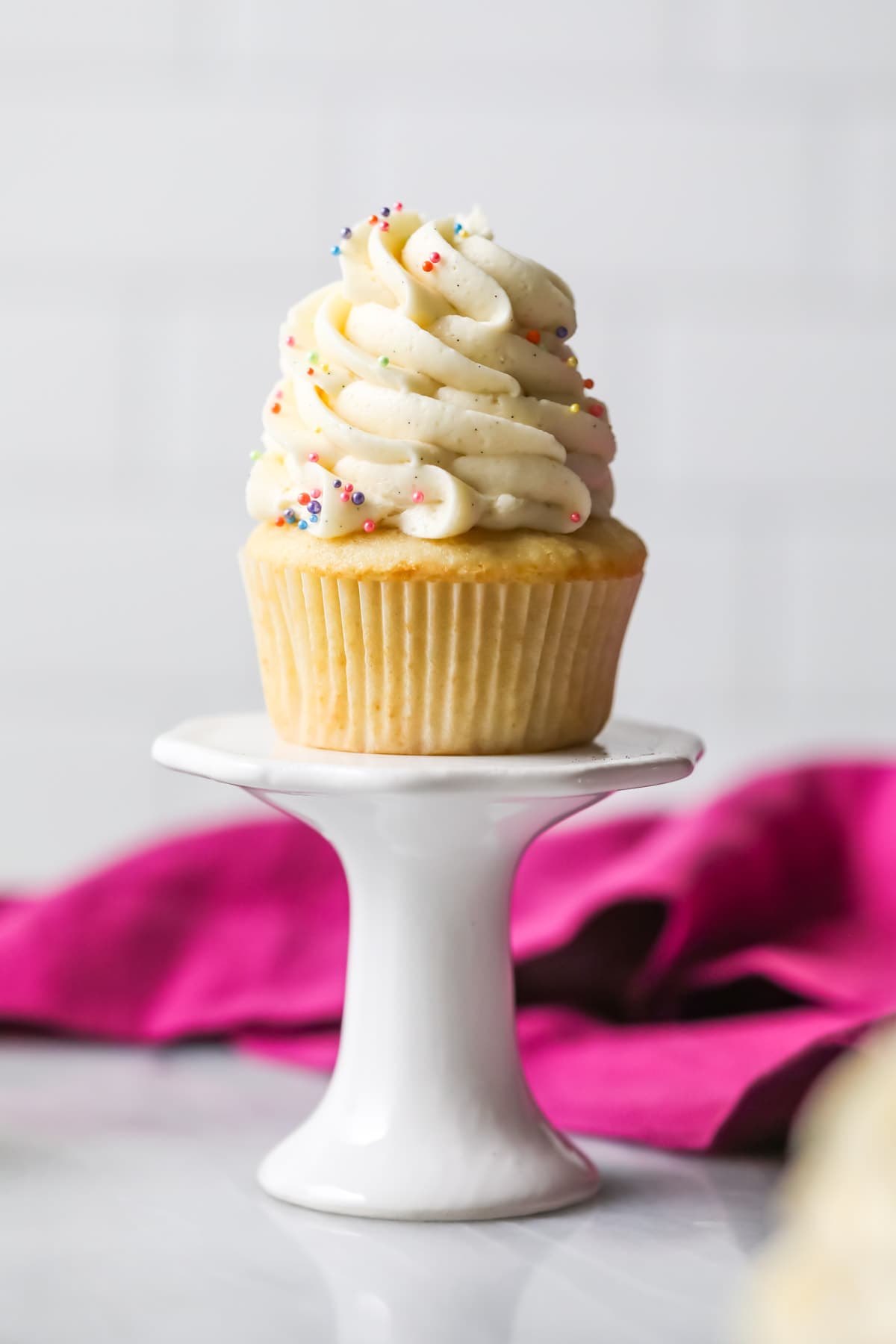 Vanilla cupcake on a pedestal topped with a tall swirl of vanilla bean frosting.