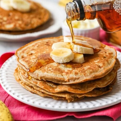 Maple syrup being poured on a stack of banana pancakes.