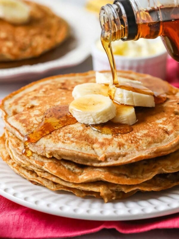Maple syrup being poured on a stack of banana pancakes.