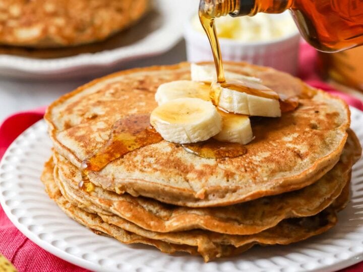 Maple syrup being poured on a stack of banana pancakes.