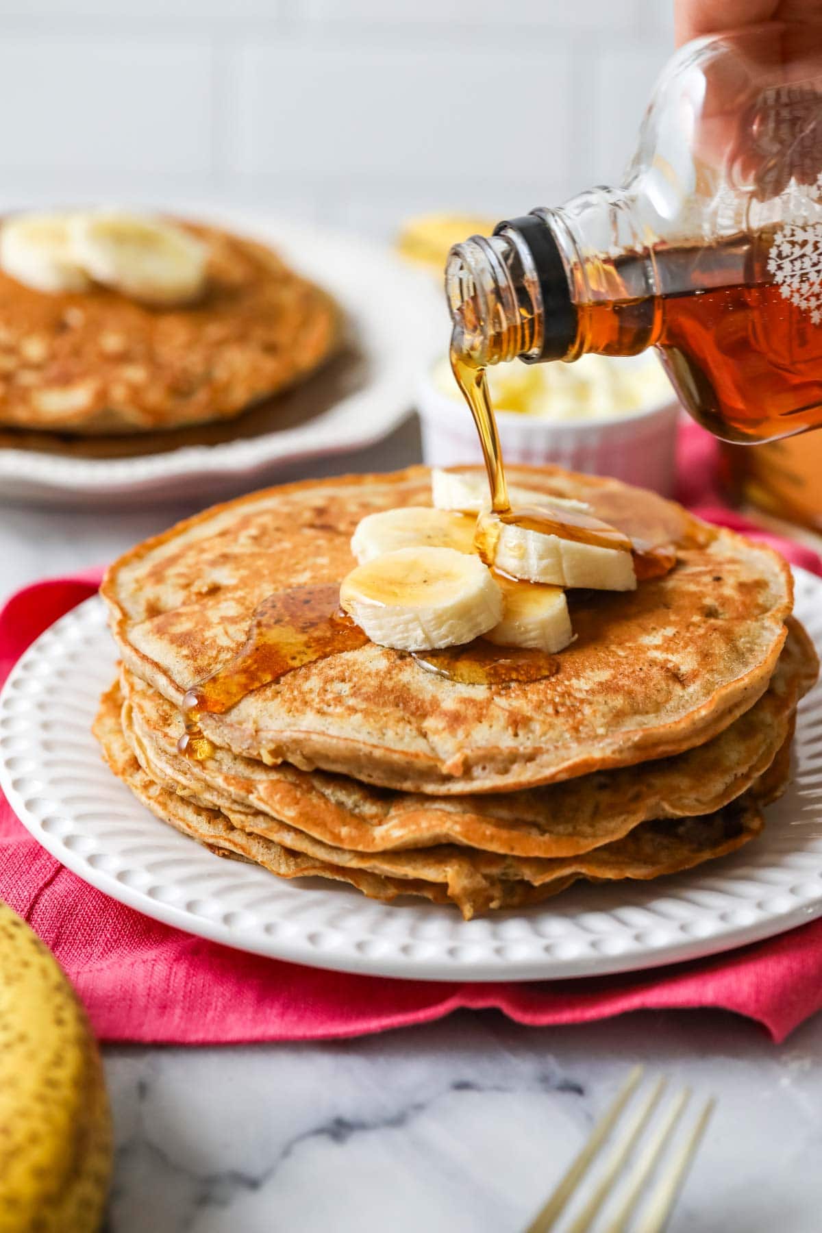 Maple syrup being poured on a stack of banana pancakes.