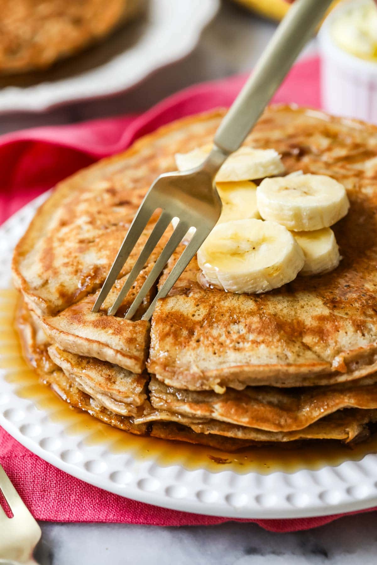 Fork pulling a bite from a stack of pancakes topped with banana slices.