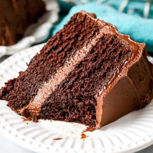 slice of chocolate cake with a bite missing (showing fudgy texture) on white plate.