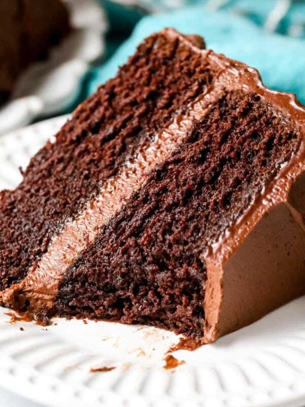 slice of chocolate cake with a bite missing (showing fudgy texture) on white plate.
