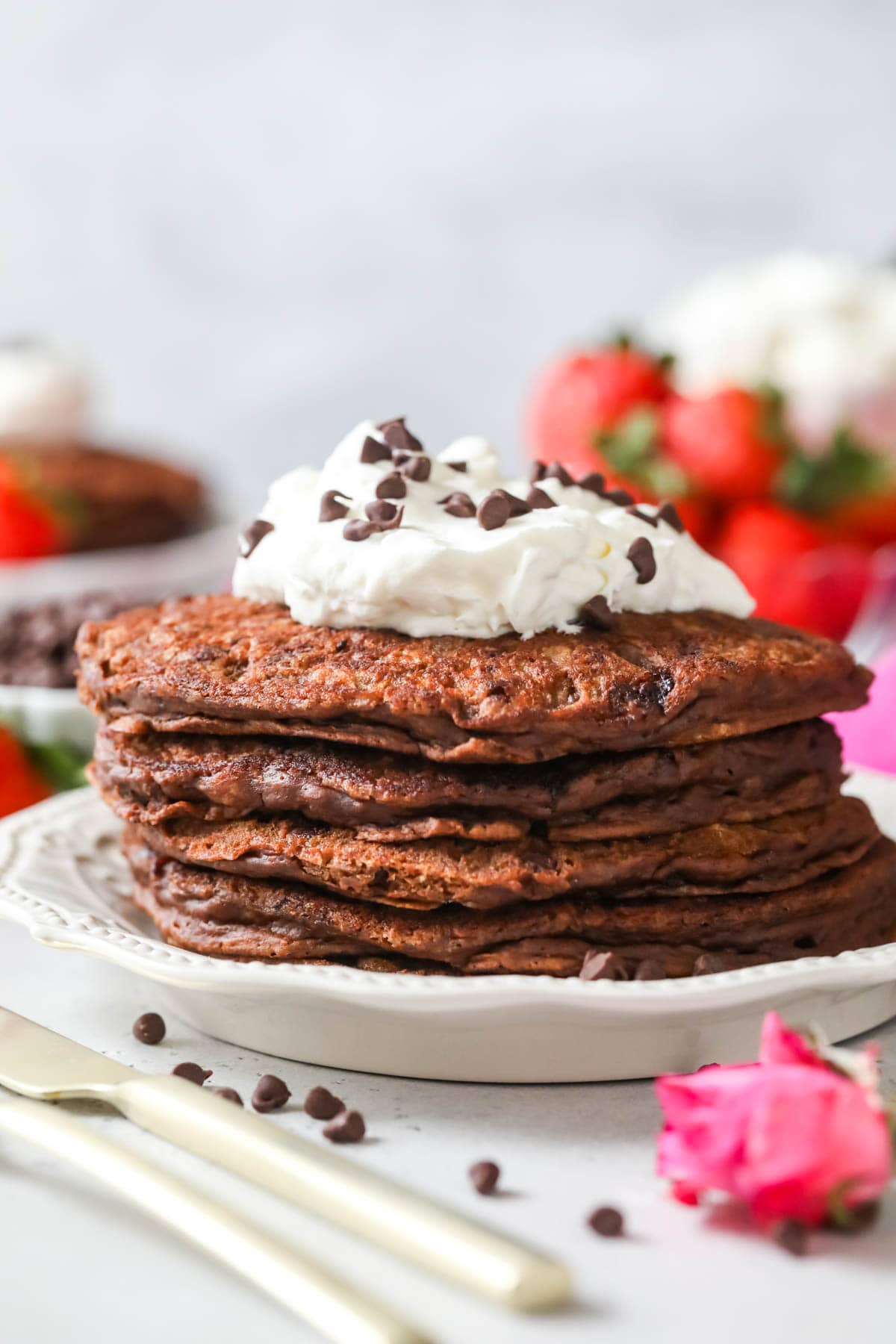 Stack of chocolate pancakes topped with whipped cream and mini chocolate chips.