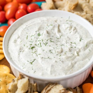 Bowl of dill dip with crackers, tomatoes, and bread surrounding it.