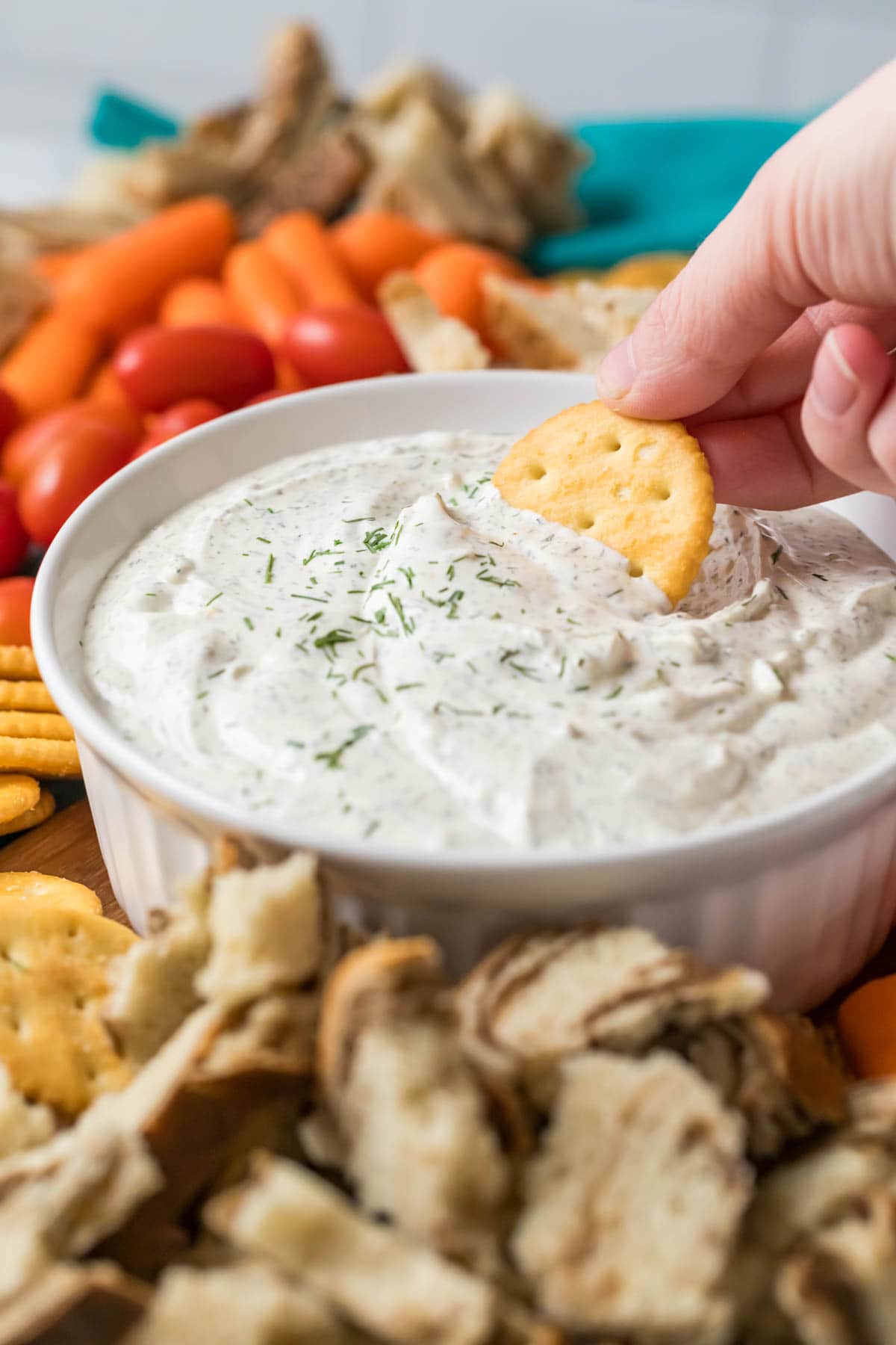 Cracker being dipped into a bowl of dill dip.
