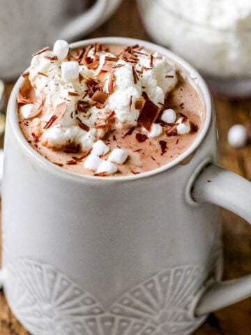 Cup of hot cocoa topped with marshmallows, whipped cream, and chocolate shavings.