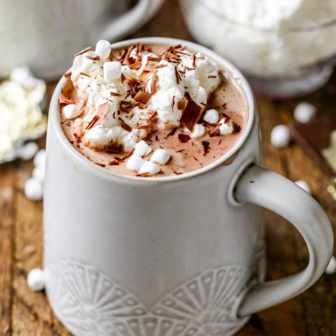 Cup of hot cocoa topped with marshmallows, whipped cream, and chocolate shavings.