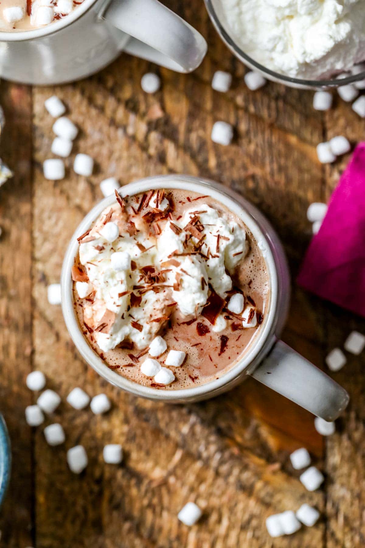 Overhead view of a cup of hot cocoa topped with marshmallows, whipped cream, and chocolate shavings.