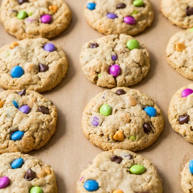 Rows of monster cookies made with colorful candies on a baking sheet.